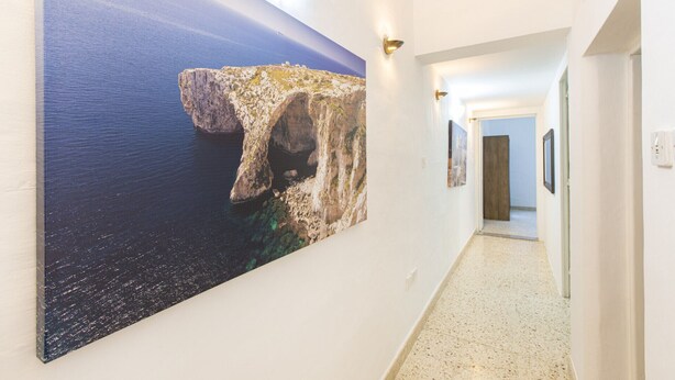 A hallway with a large painting of a rocky coastline, a light-colored floor, and a door at the end.