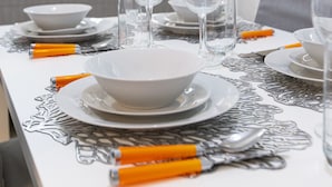 A dining table set with plates, bowls, and wine glasses, with orange-handled cutlery and a decorative table runner.