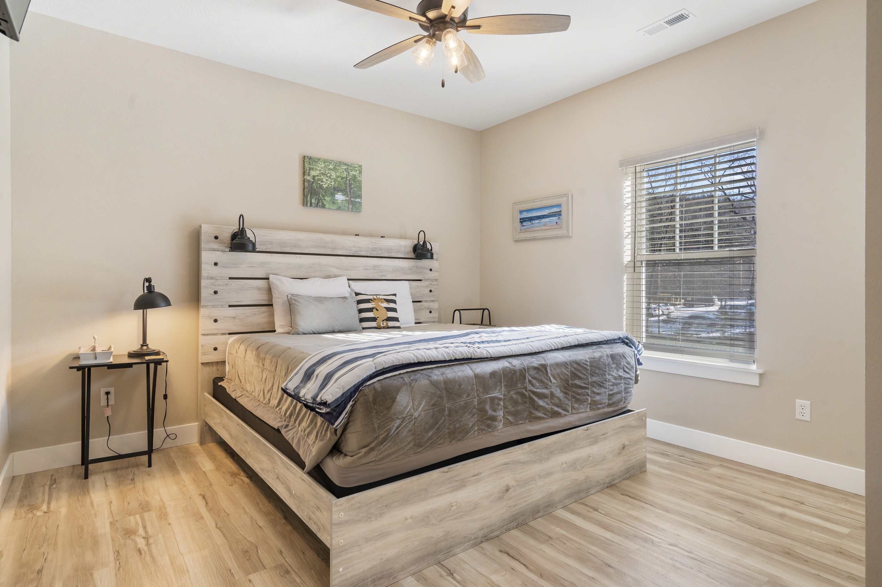 A bedroom with a wooden bed, a ceiling fan, a bedside table with a lamp, and a window with blinds.