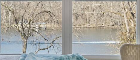 A bedroom with a large window overlooking a river and trees.