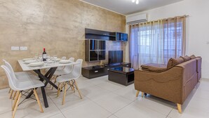 A modern living room with a dining area, a sofa, and a TV. - Modern 2-Bedroom Maisonette in Swieqi (Swieqi)
