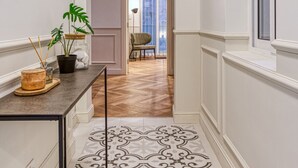 A narrow hallway with a patterned floor, a table with a potted plant, and a chair in the background. - Valletta in Style beautiful apartment (IL-BELT VALLETTA)