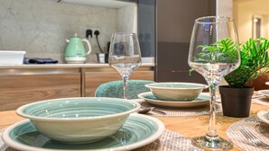 A dining table with plates, bowls, and wine glasses. There is a green plant in a pot and a green kettle in the background. - Valletta in Style beautiful apartment (IL-BELT VALLETTA)