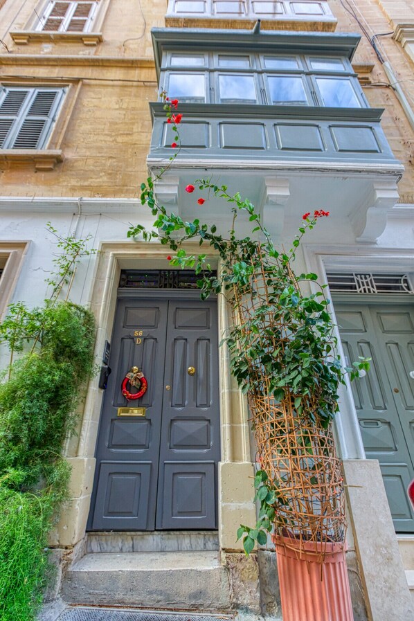 A building facade with a dark gray double door, a red wreath, and a climbing plant with red flowers.