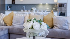 Een moderne woonkamer met een grijze bank, kussens in wit en geel, en een tafel met een witte bloemstelling.