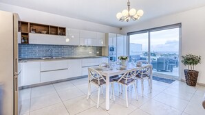 Een moderne keuken met witte kasten, een blauwe betegelde achterwand en een eethoek met een witte tafel en stoelen.