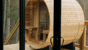 A wooden cylindrical structure with a bench inside, situated on a wooden deck with a railing.