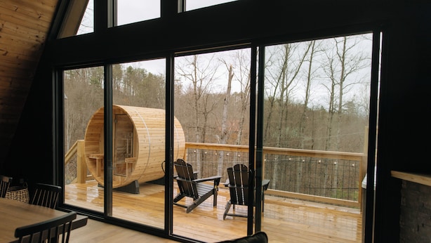 A wooden cabin with large windows, a deck, and two chairs.