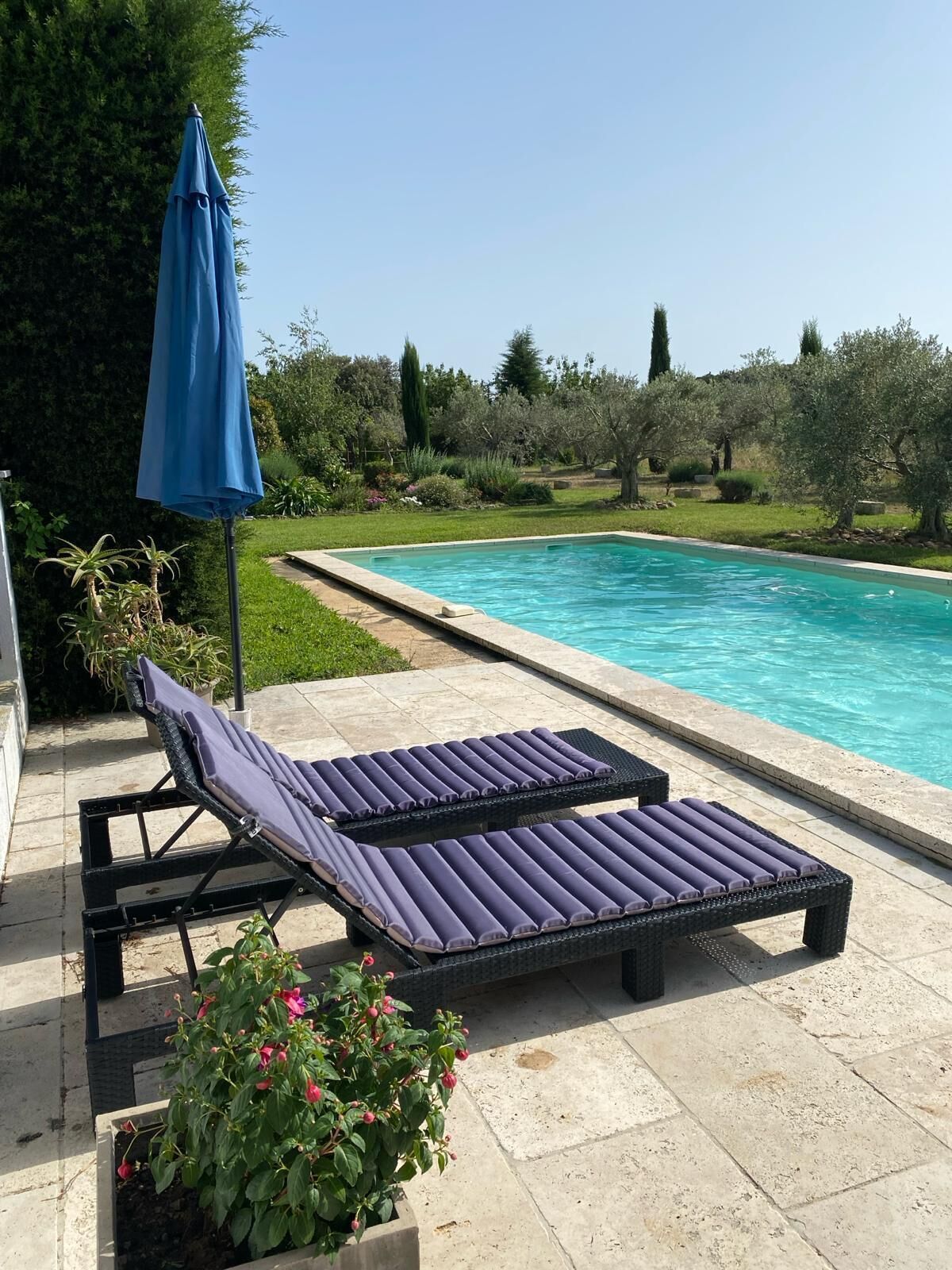 A swimming pool with two lounge chairs and a blue umbrella.