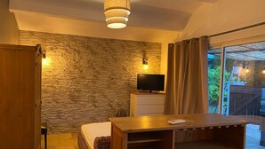A cozy room with a stone wall, a television, a wooden table, and a large window with curtains. - Tamarind Duo (Arles)