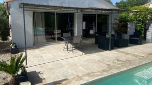 A covered patio area with a pool, outdoor furniture, and a sliding glass door leading to an interior space. - Tamarind Duo (Arles)