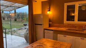 A kitchen with a wooden table, a refrigerator, a dishwasher, and a window overlooking a garden. - Tamarind Duo (Arles)