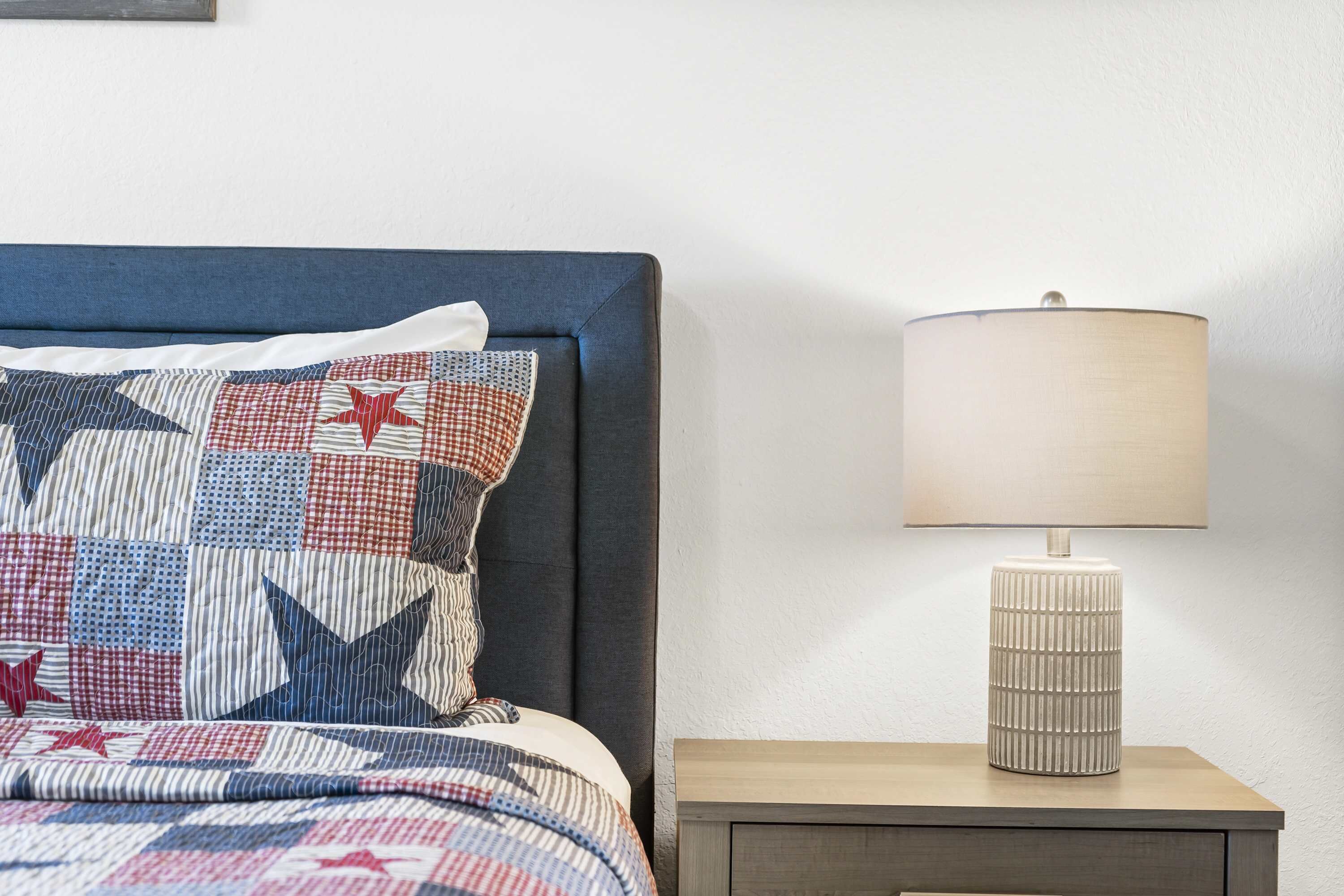 A neatly made bed with a star-patterned quilt, a bedside lamp, and a wooden nightstand.
