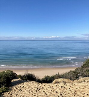 Ein Strand mit blauem Himmel, ruhiger See und sandigem Untergrund.