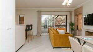 A modern living room with a sofa, a dining table, and a TV. - Stunning 2 bedroom apartment in Herdade da Aroeira (Almada)