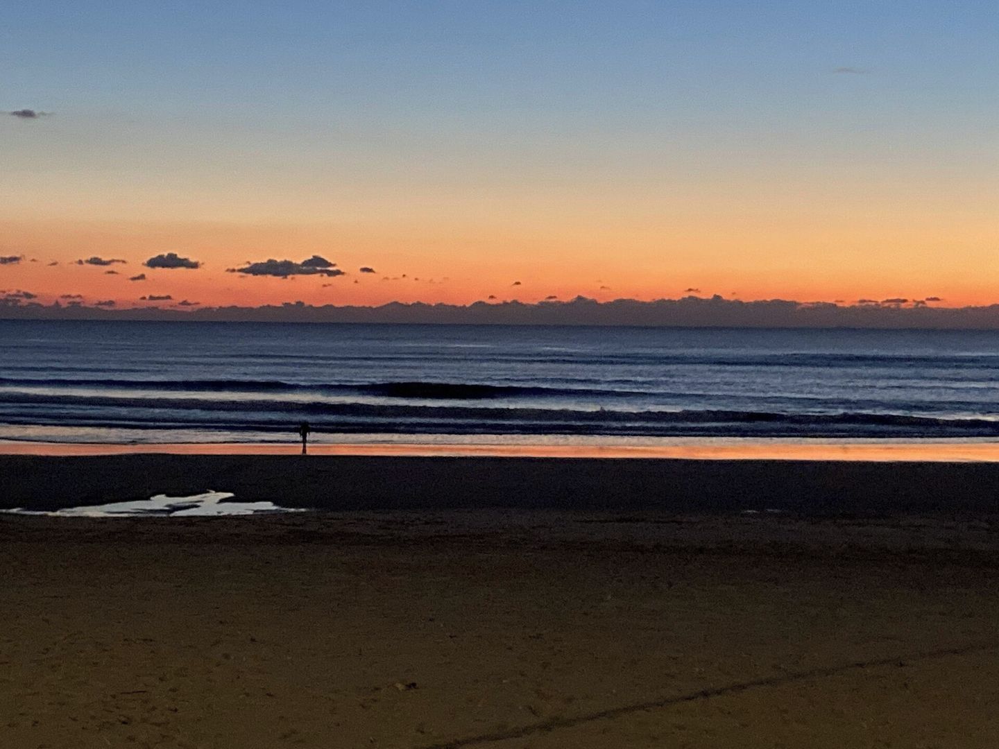 En strand med klar himmel og rolig sø ved solnedgang.
