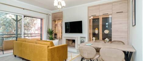 Una sala de estar moderna con sofá, mesa de comedor, sillas, televisor de pantalla plana y chimenea.