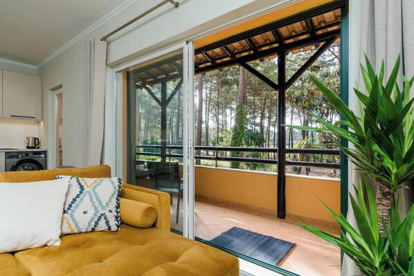 A room with a sofa, a dining table, and a view of a balcony with a railing.