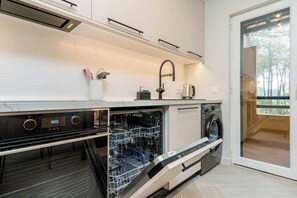 Cocina moderna con electrodomésticos integrados, incluyendo lavavajillas y horno, y una puerta corrediza de vidrio que da a un espacio exterior.