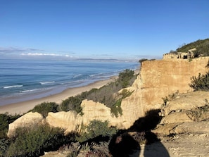 A coastal landscape with a cliff overlooking the beach and ocean.
