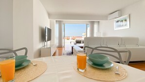A modern living room with a sofa, a dining table with a glass of orange juice, and a TV mounted on the wall. - Penthouse Triplex com Jacuzzi T3 Hsrentals Vilama (Loulé)