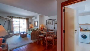 Una sala de estar con comedor, un sofá, una mesa de centro y una puerta que da a un cuarto de lavado.