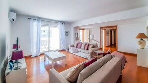 Een ruime woonkamer met een bank, salontafel en lamp. Er is een schuifdeur naar een buitenruimte.