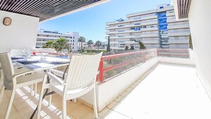 Een balkon met een witte tafel en stoelen, met uitzicht op een stadsgezicht met moderne gebouwen en palmbomen.