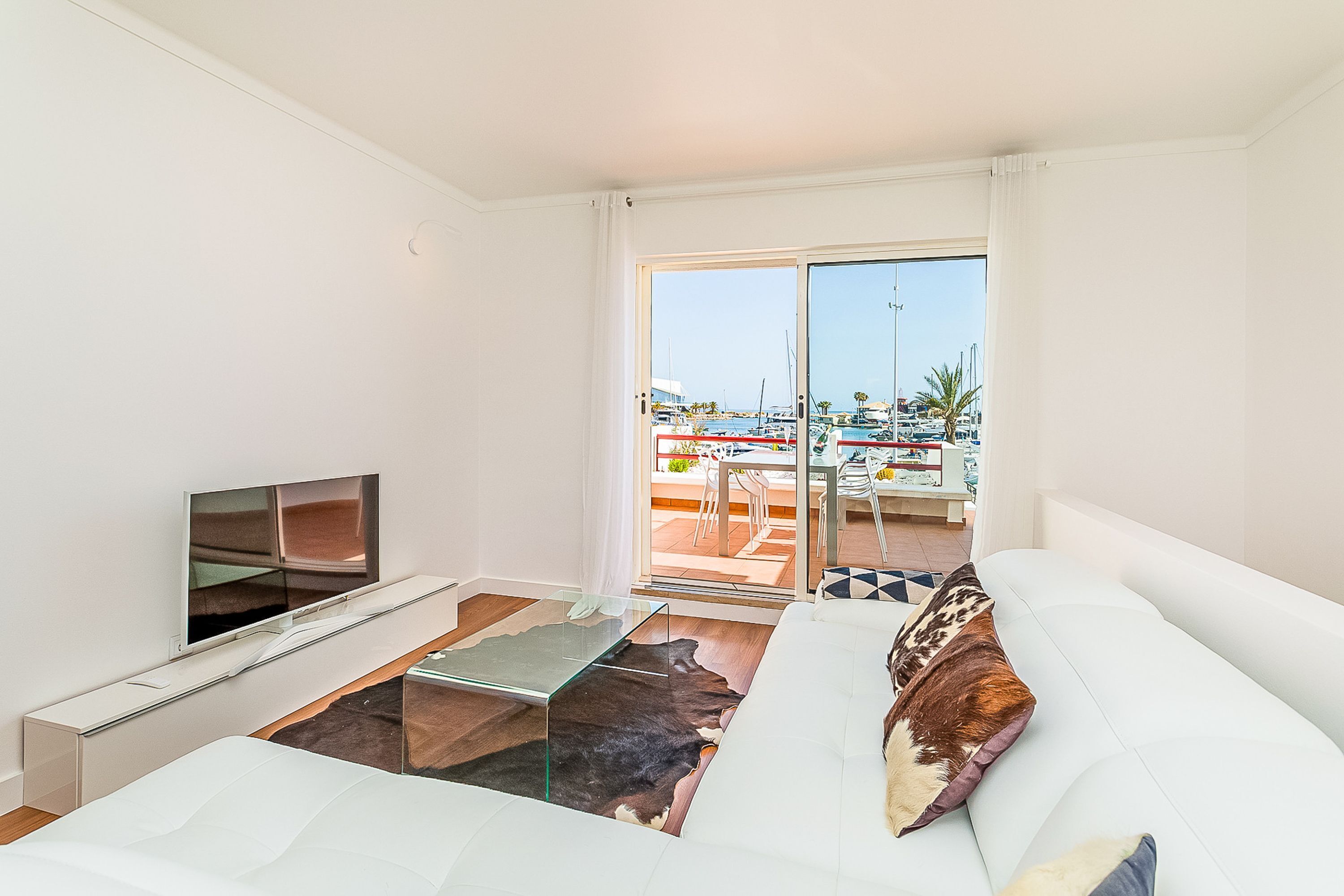 A modern living room with a sofa, a flat-screen TV, and a glass coffee table.