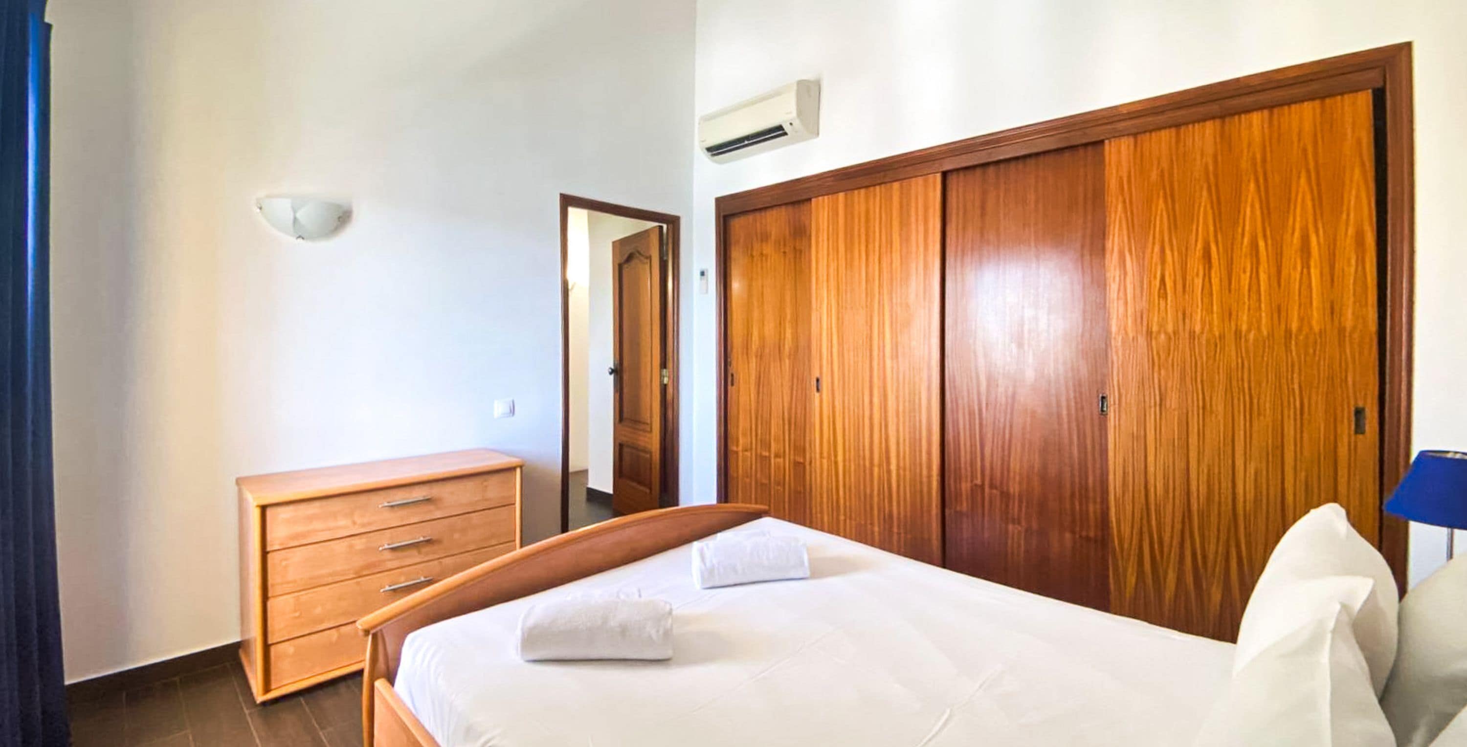 A bedroom with a wooden bed, a wooden dresser, a wardrobe, and a mirror.