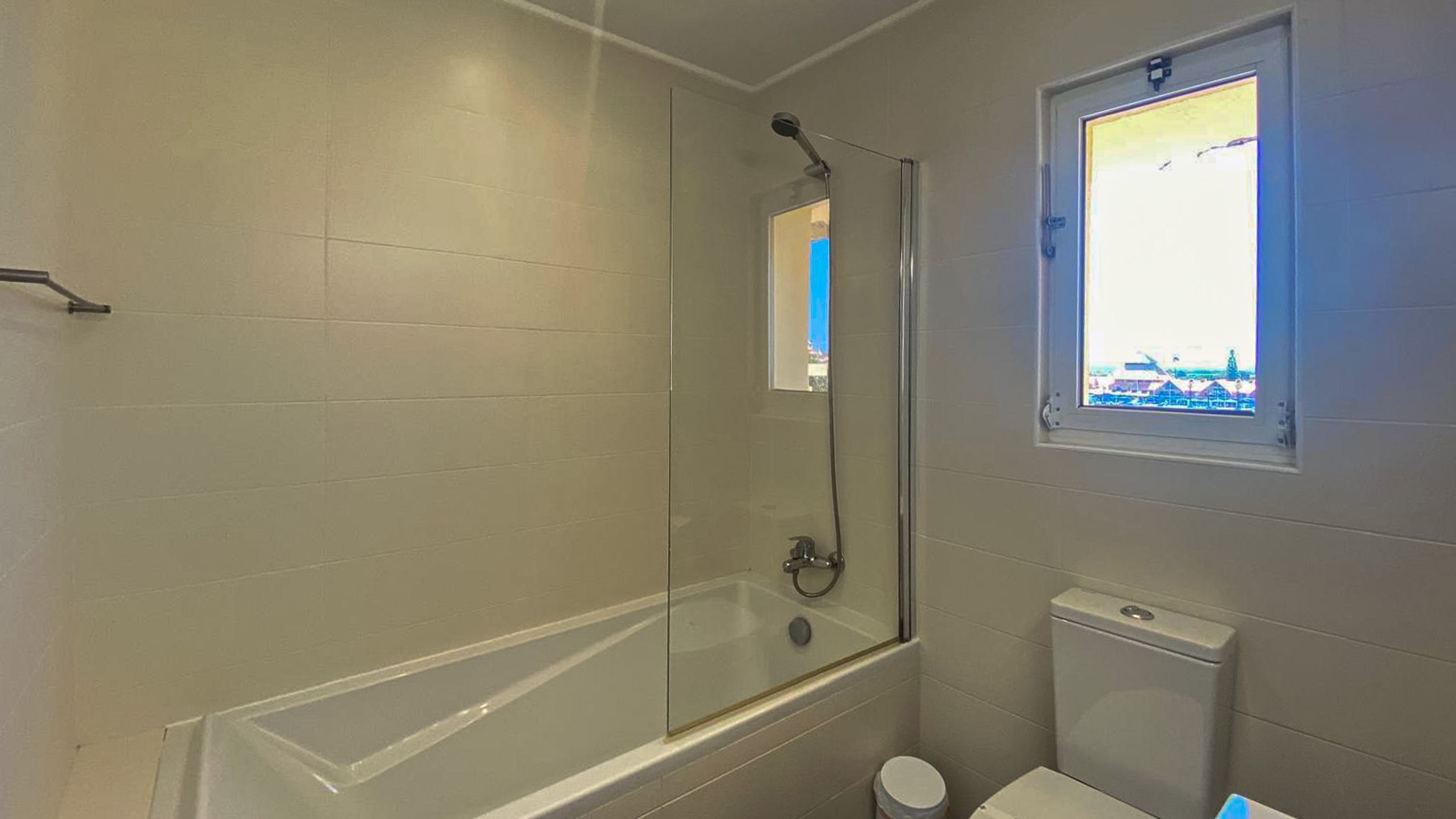 Une salle de bain avec une douche à parois de verre, des toilettes et une fenêtre donnant sur un immeuble.