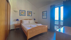 A hotel room with a wooden bed, two bedside tables with lamps, and three framed floral paintings on the wall. - Duplex Marina Plaza T1 Hsrentals (Loulé)