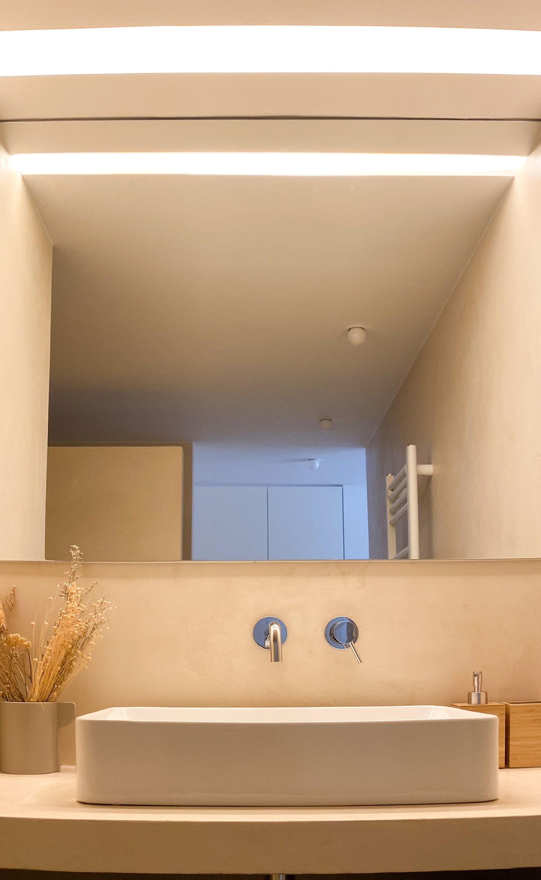 Ein modernes Badezimmer mit einem großen Spiegel, einem weißen Waschbecken und einem Handtuchhalter.