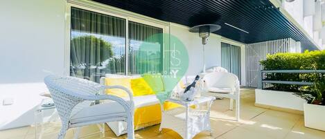 A modern outdoor seating area with wicker chairs and a yellow sofa, a table with a bottle, and a lamp.