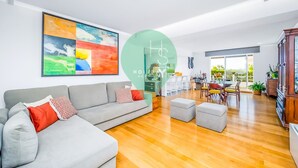 A modern living room with a grey sectional sofa, a dining area with a table and chairs, and a large abstract painting on the wall. - Ref gio Sereno Marina T2 Hsrentals Vilamarina (Loulé)