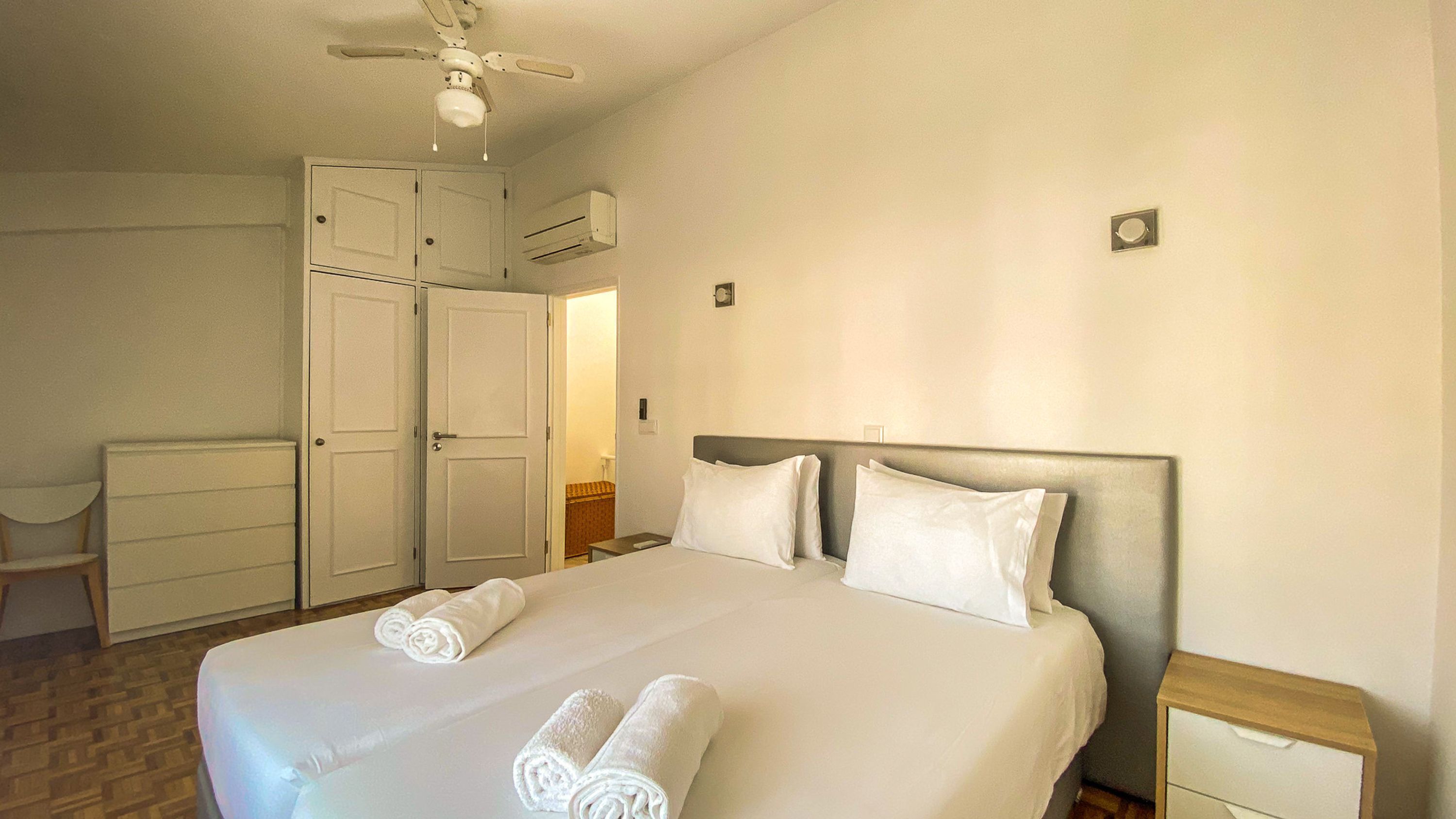 Una habitación de hotel con una cama, dos mesitas de noche, un ventilador de techo y un armario.