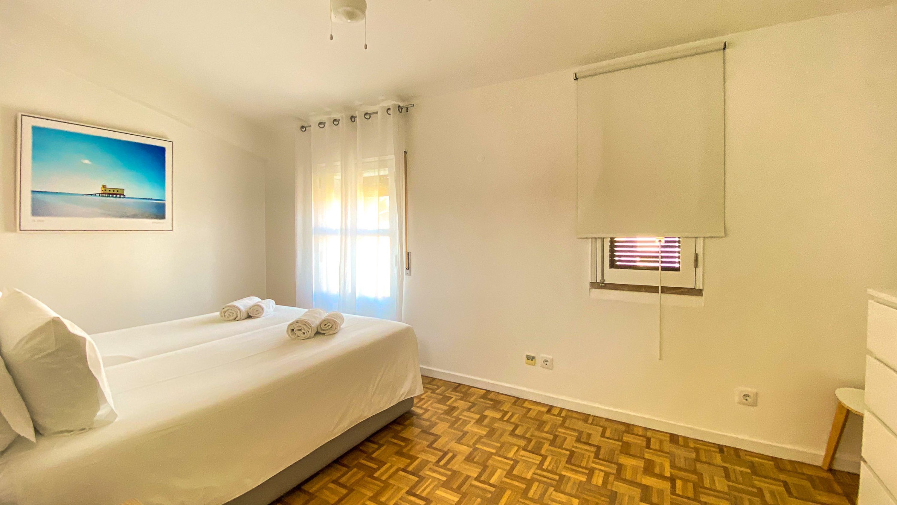 Una camera d'albergo con un letto, una finestra con persiane, un quadro appeso al muro e un pavimento in legno.