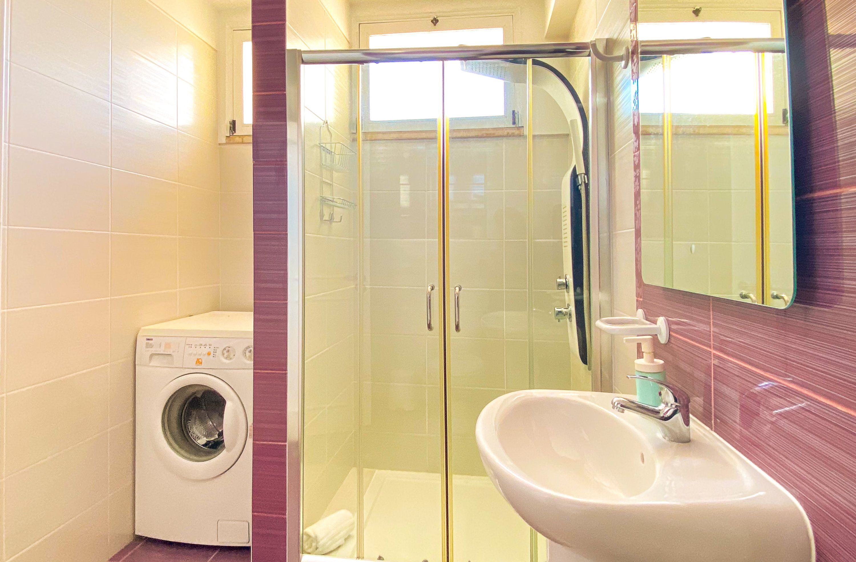 Un bagno funzionale con lavatrice, doccia trasparente e lavandino con specchio.