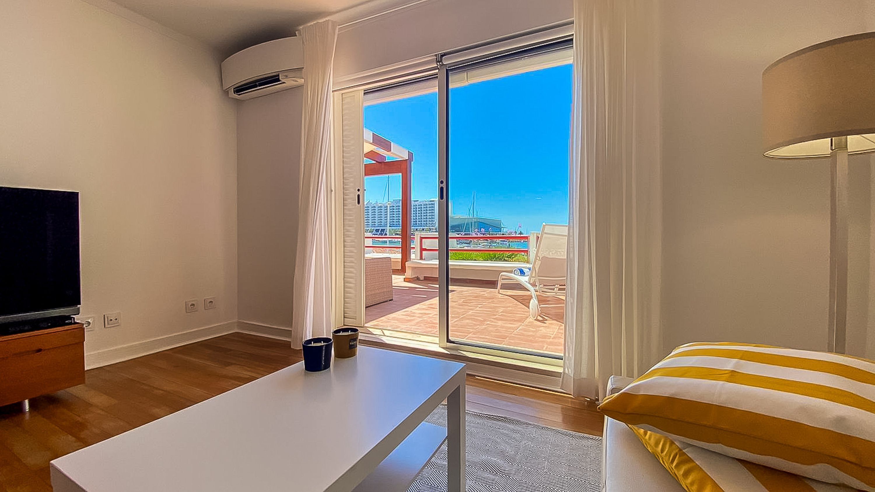 Una camera d'hotel con un'ampia porta-finestra scorrevole che si apre su uno spazio esterno con vista su barche ed edifici.