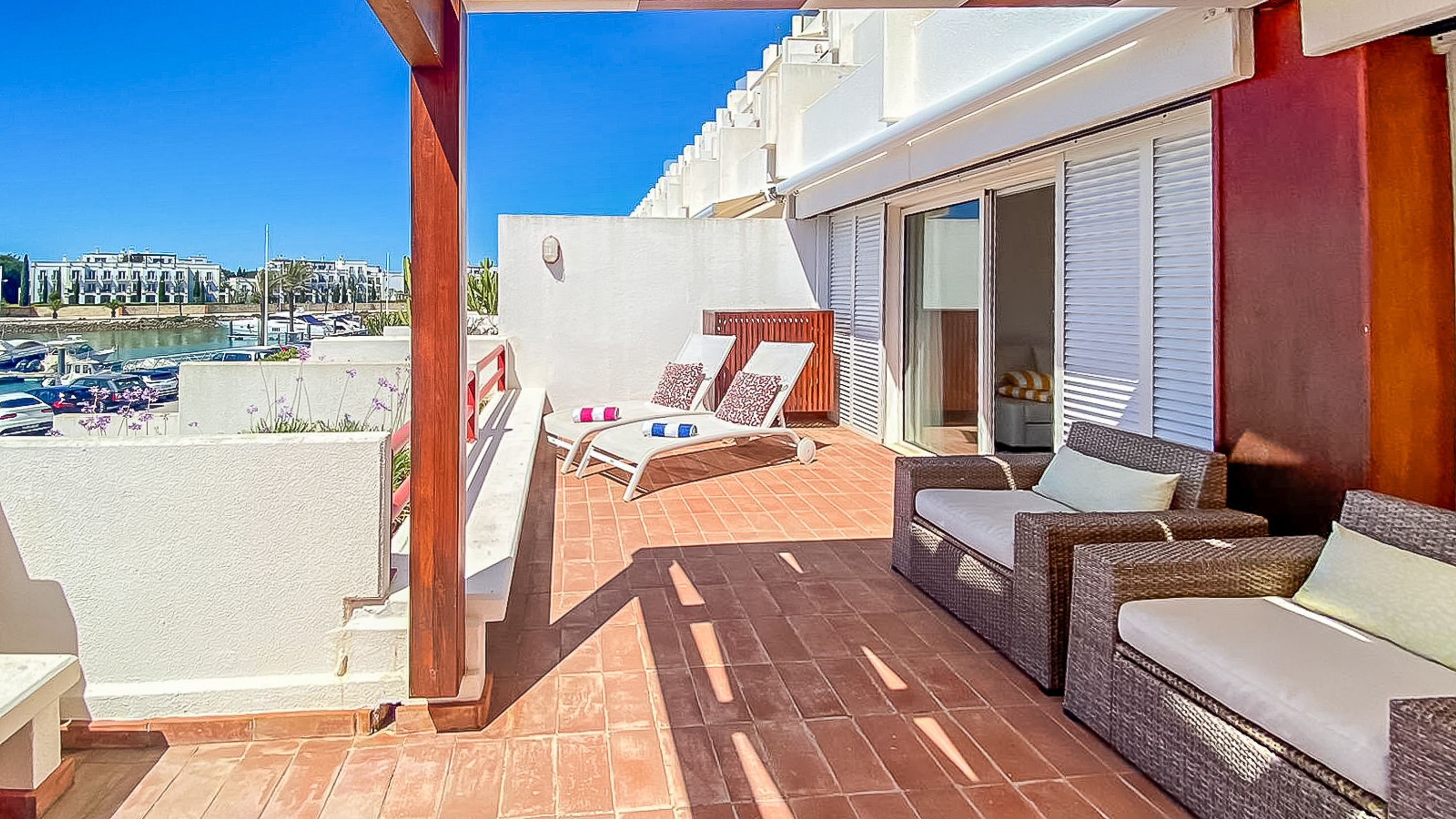 A balcony with two lounge chairs, a wicker sofa, and a view of a marina.
