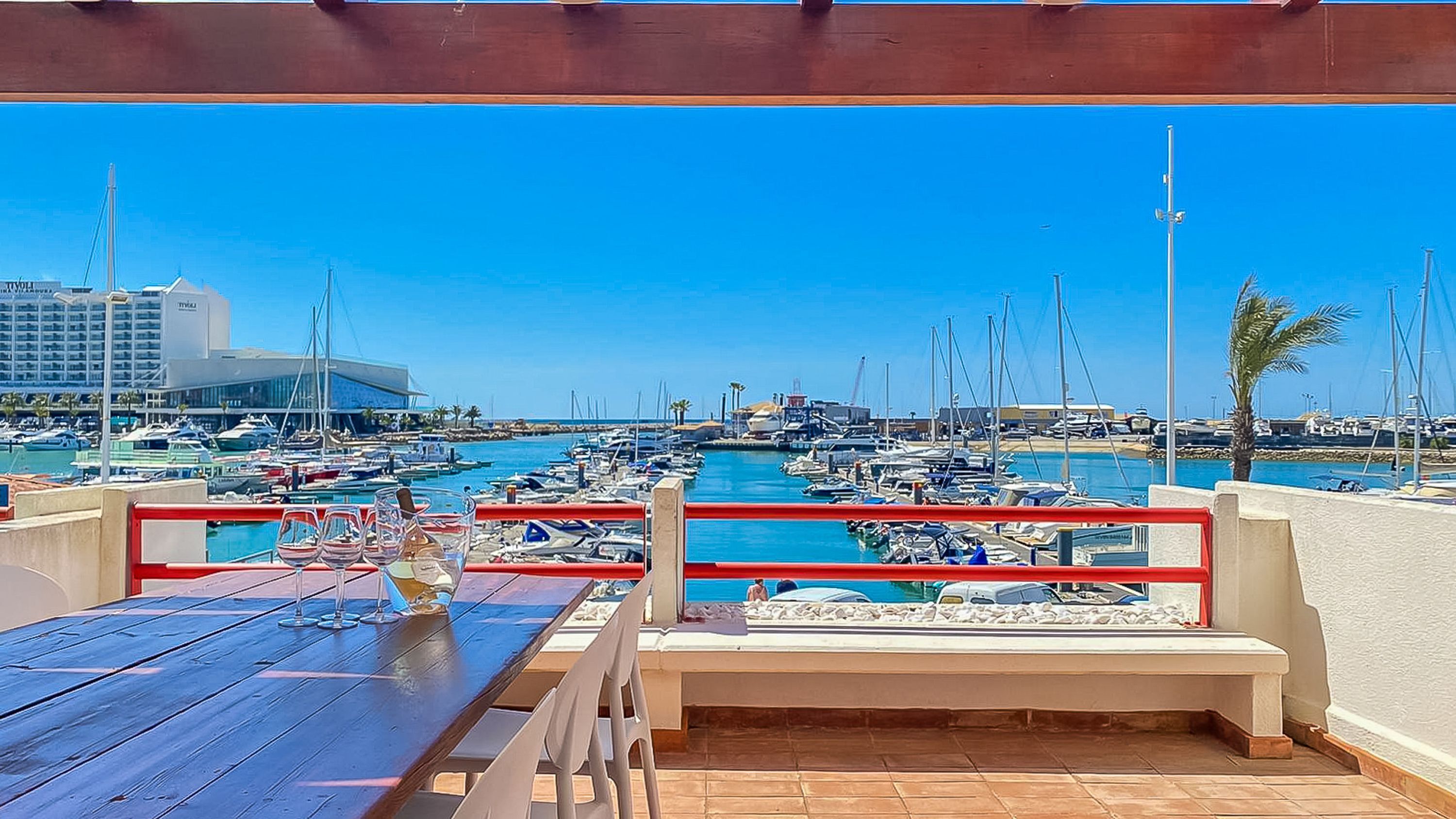 A marina with boats, a building in the background, and a table with chairs in the foreground.