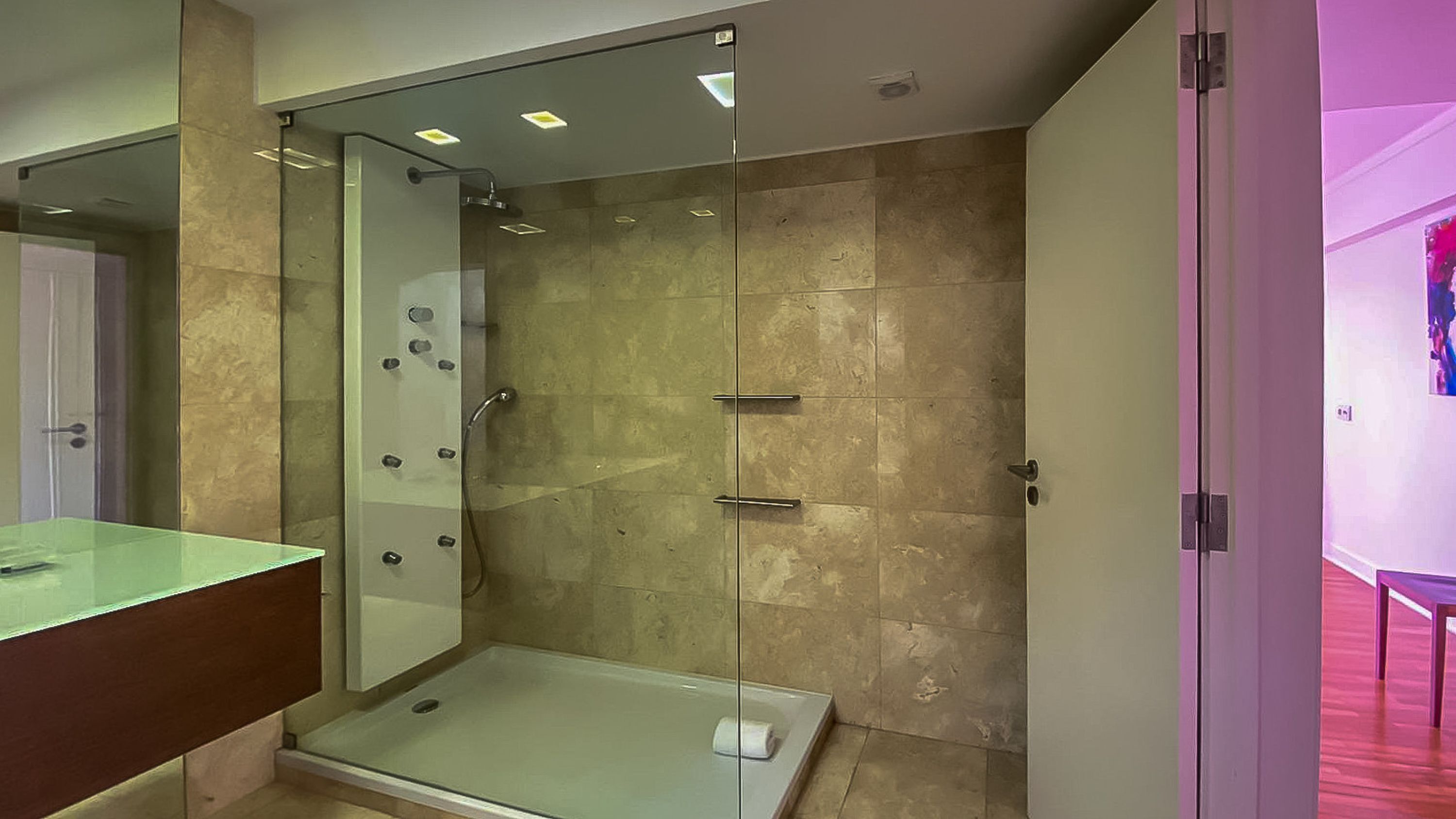 A modern bathroom with a glass-enclosed shower, a glass vanity, and beige tiles.