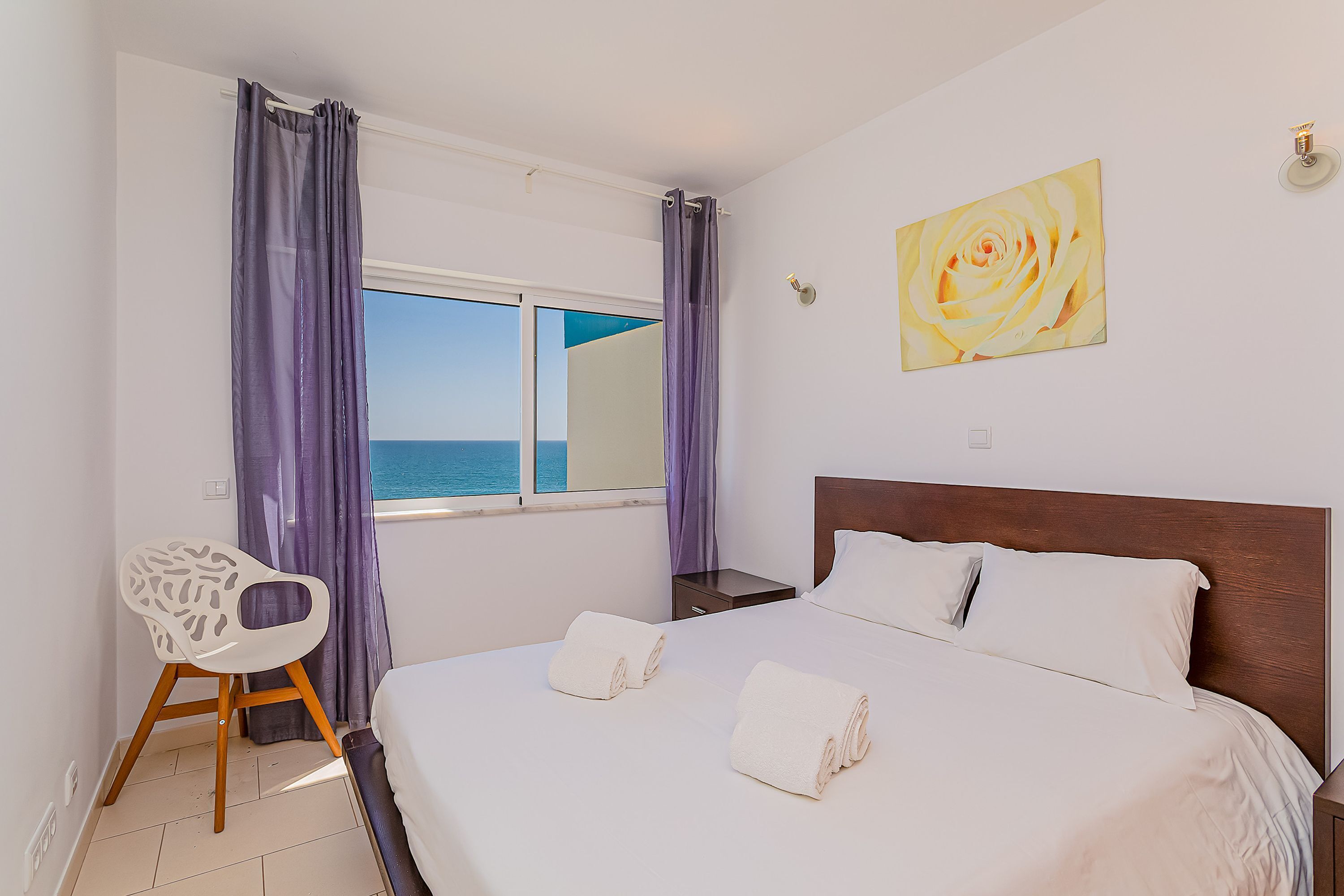 Een hotelkamer met een bed, een stoel, een raam met gordijnen en een schilderij aan de muur.
