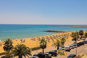 Una playa con coches aparcados, sombrillas y palmeras.