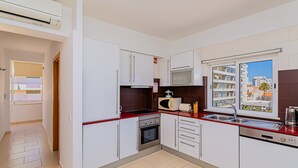 Una cocina moderna con armarios blancos, encimera roja, microondas integrado, tostadora, fregadero y horno.