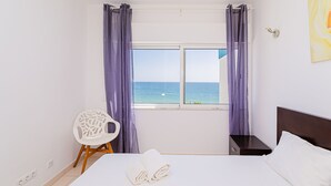 Un dormitorio con cama, una silla, una mesita de noche y una ventana con cortinas.