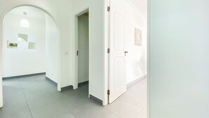 Un pasillo con paredes blancas, piso de baldosas y una puerta con panel decorativo.