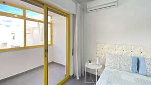 Habitación de hotel con cama, una mesita, una planta en maceta y vistas amplias por una ventana grande.