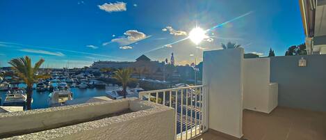 Ein Balkon mit Blick auf einen Yachthafen und Boote, ein klarer Himmel und ein Gebäude im Hintergrund.