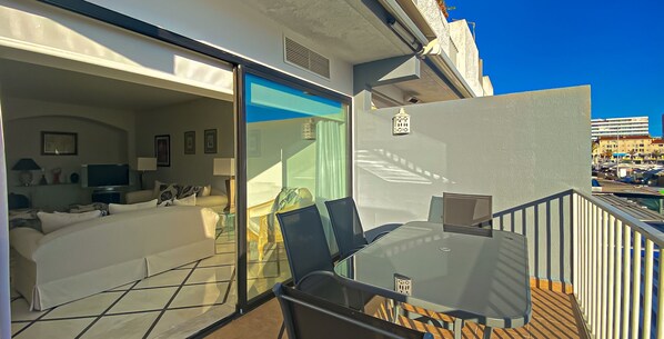 A balcony with a glass door leading to a room with a bed, a chair, and a table.